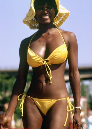 Негритянка в бикини и шляпе от солнца направляется в лес, чтобы раздеться догола