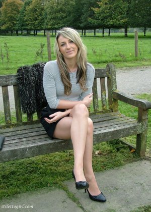Модель с ножками позирует на деревенской скамейке в черной юбке и туфлях-лодочках